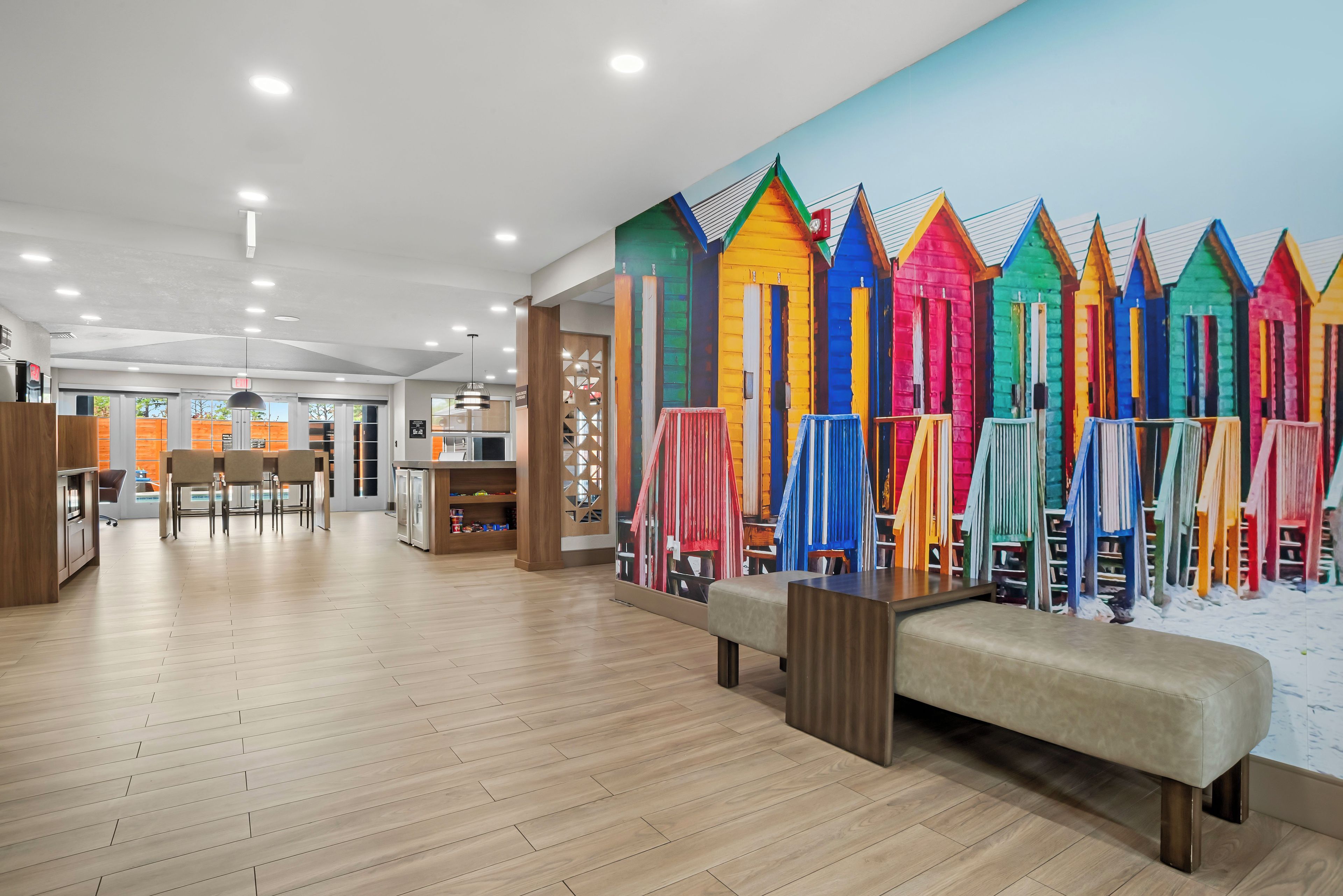 Un intérieur moderne avec un plancher en bois, un coin salon et une fresque colorée représentant des cabanes de plage.