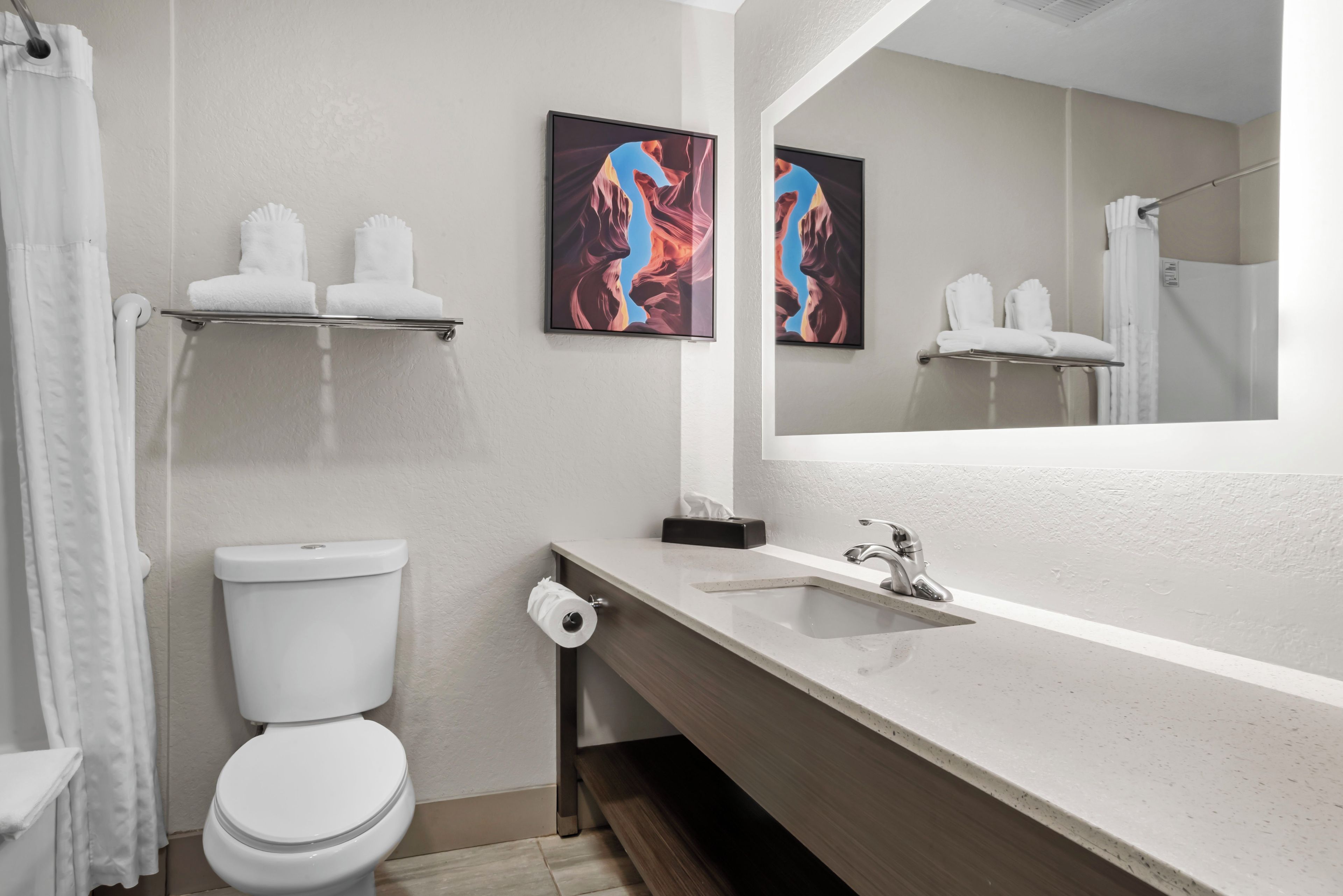 Une salle de bain comprenant des toilettes, un lavabo, un miroir et deux tableaux encadrés accrochés au mur.