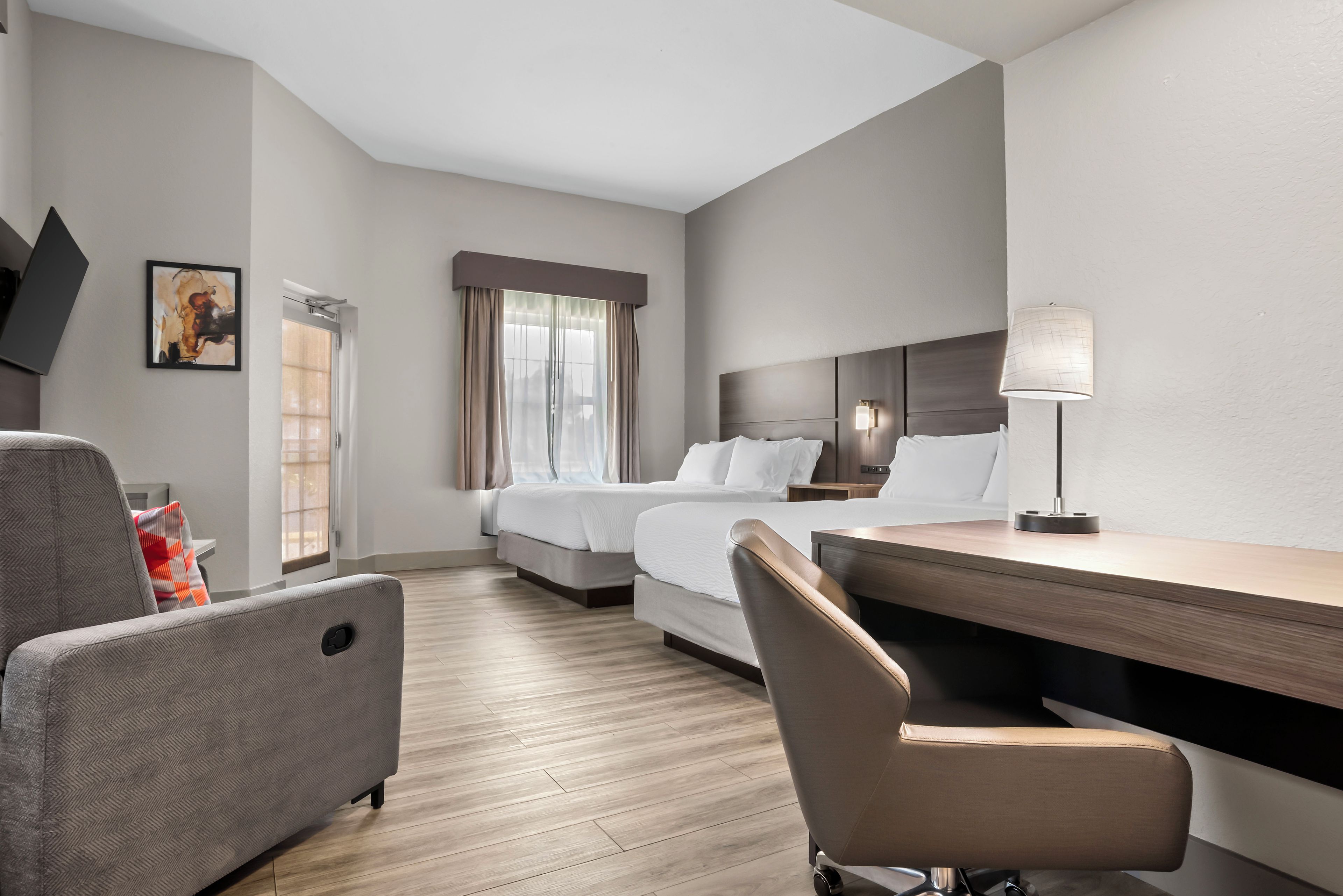 Habitación de hotel con cama, escritorio, silla, lámpara y un cuadro en la pared.
