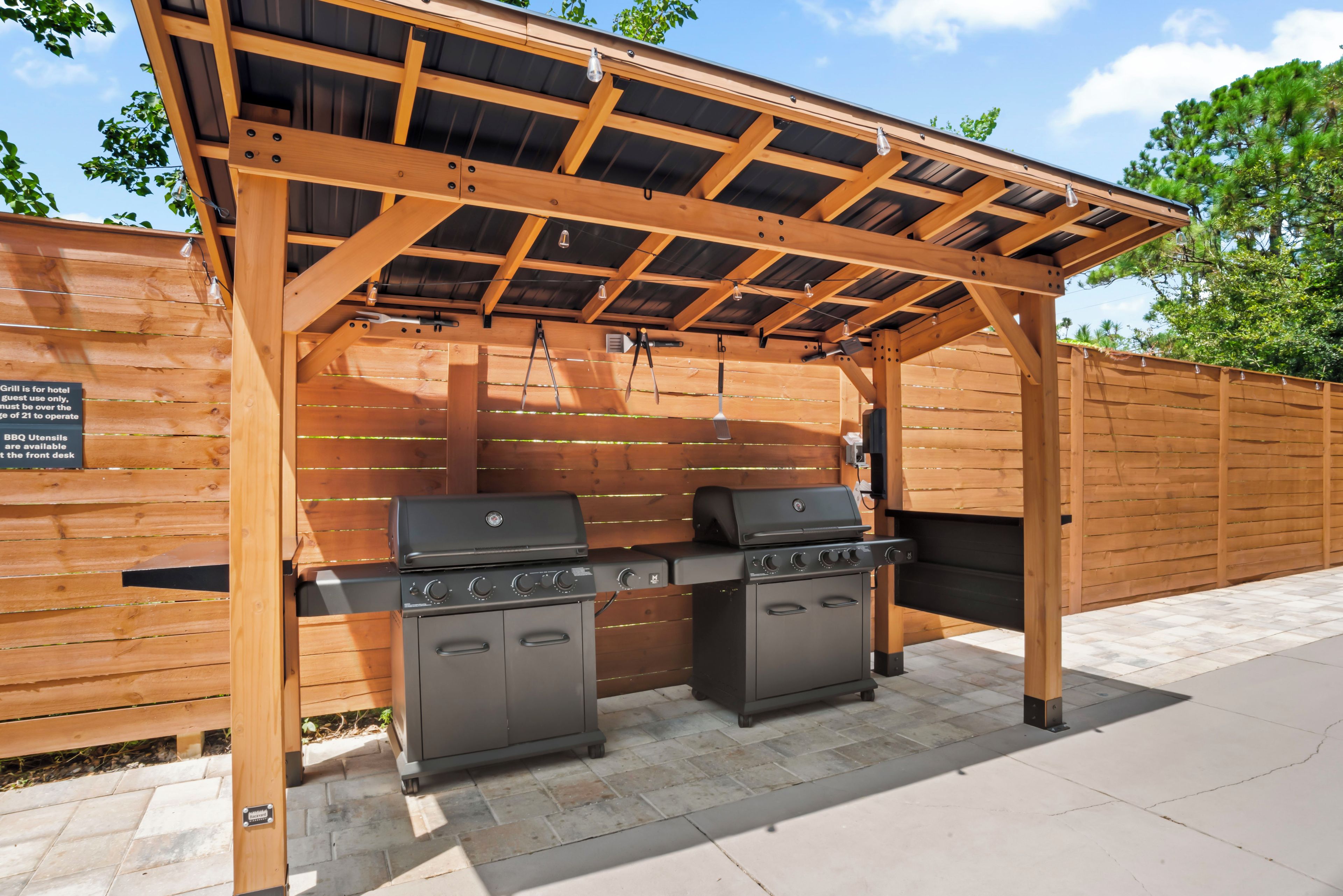 Un espace barbecue extérieur équipé de deux grils, surmonté d’une pergola en bois, et agrémenté d’un panneau indiquant que les grils sont réservés à l’usage exclusif des clients de l’hôtel.