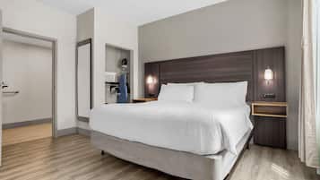 A modern hotel room with a large bed, wooden flooring, a wardrobe, and a nightstand with a lamp.