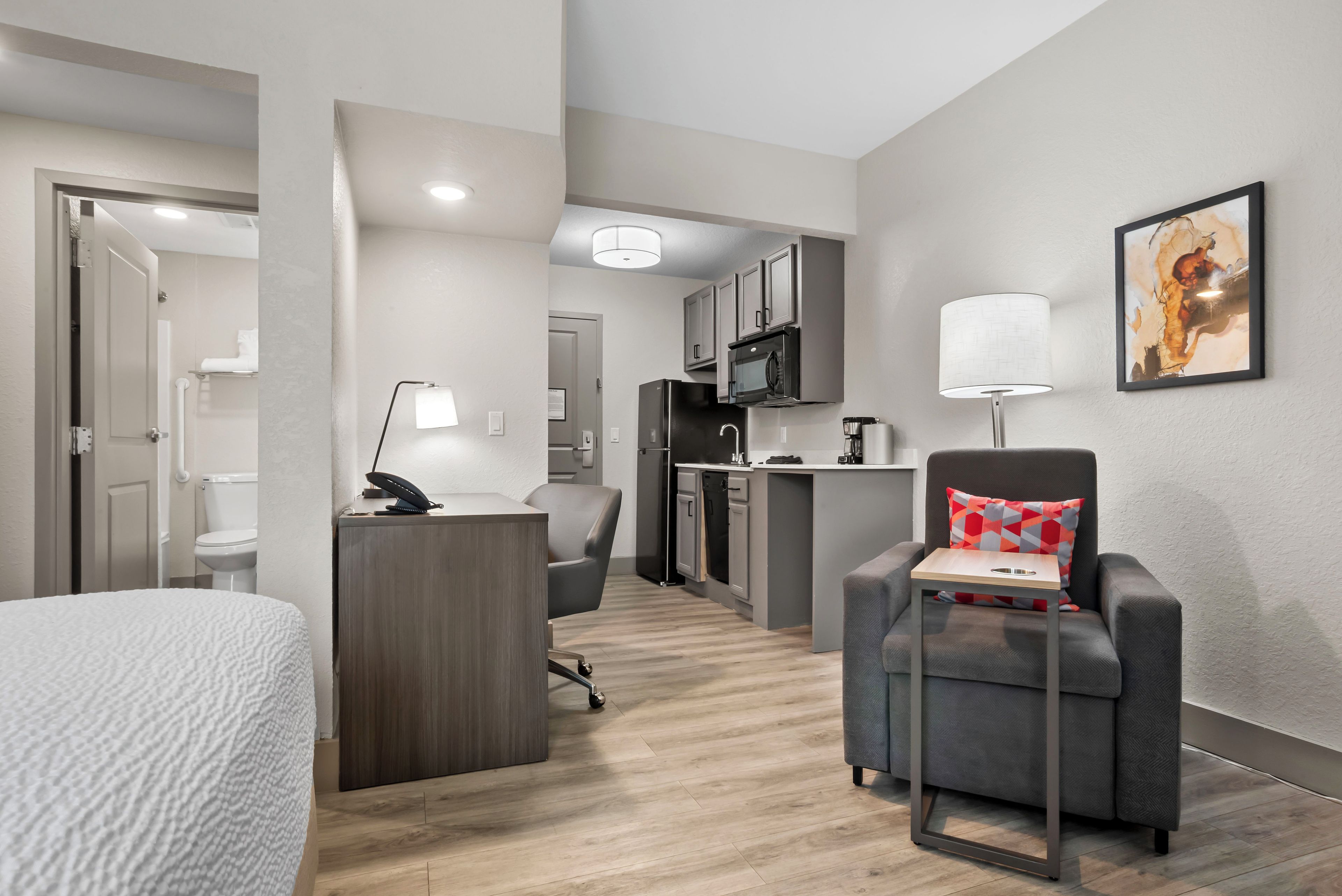 Habitación de hotel moderna con cama, escritorio, silla, kitchenette y baño.