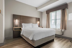 Una habitación de hotel moderna con una cama grande, mesitas de noche con lámparas, una ventana con cortinas y un equipo de aire acondicionado integrado.