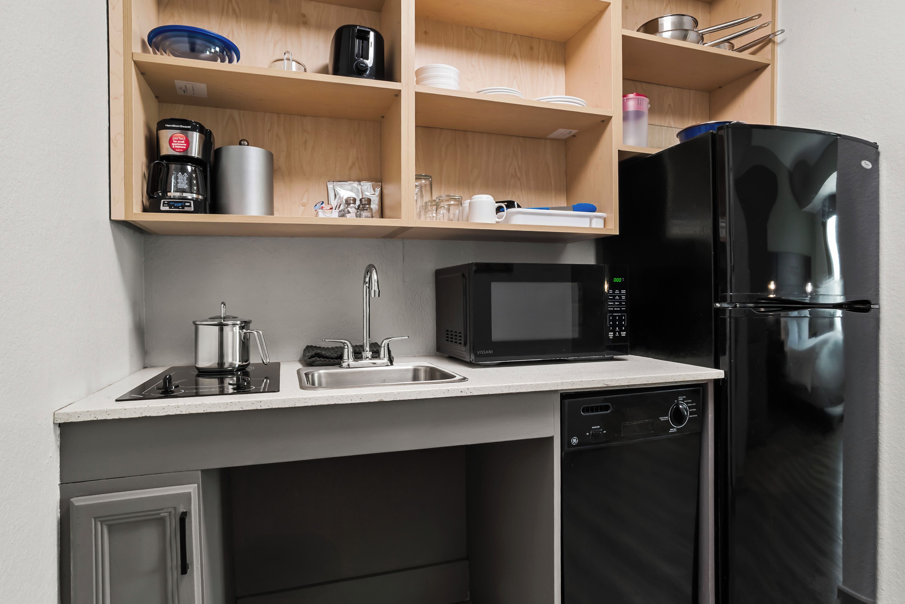 A compact kitchen with a black refrigerator, a microwave, a coffee maker, and a sink.