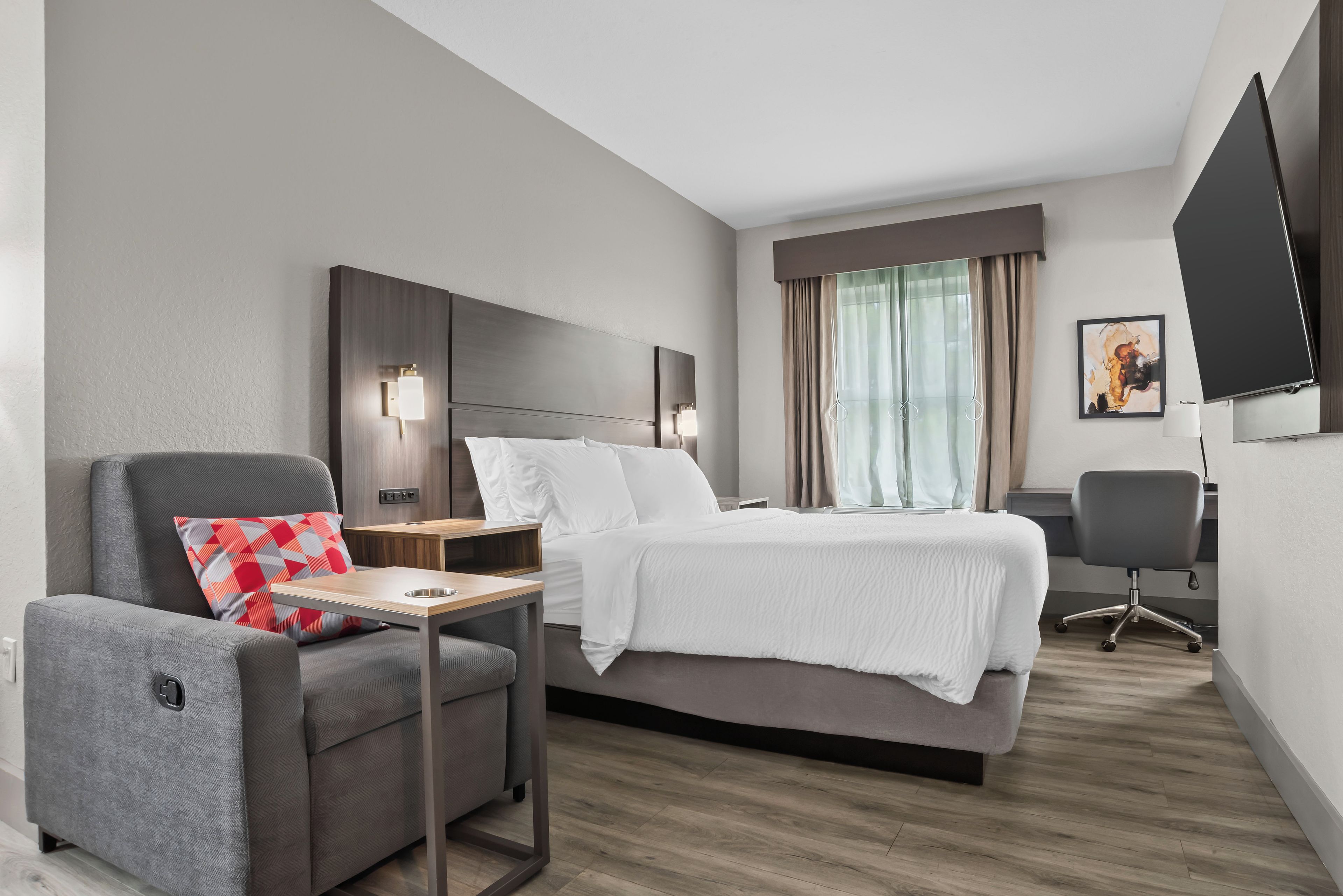 Habitación de hotel con cama, escritorio, silla, televisor y ventana con cortinas.