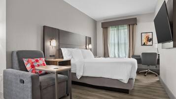 Habitación de hotel con cama, escritorio, silla, televisor y ventana con cortinas.