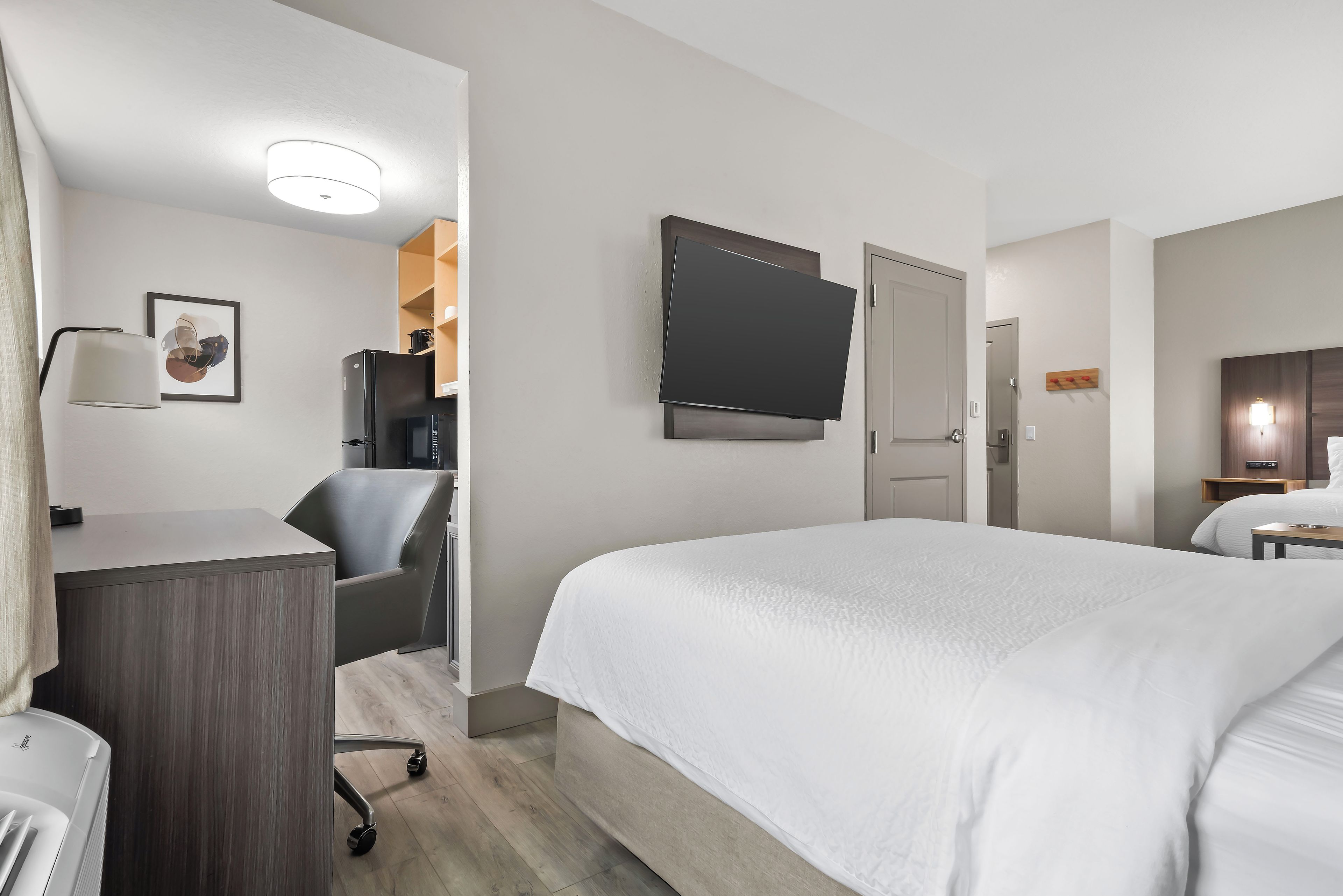 Quarto de hotel com cama, escrivaninha, cadeira, televisão e porta.