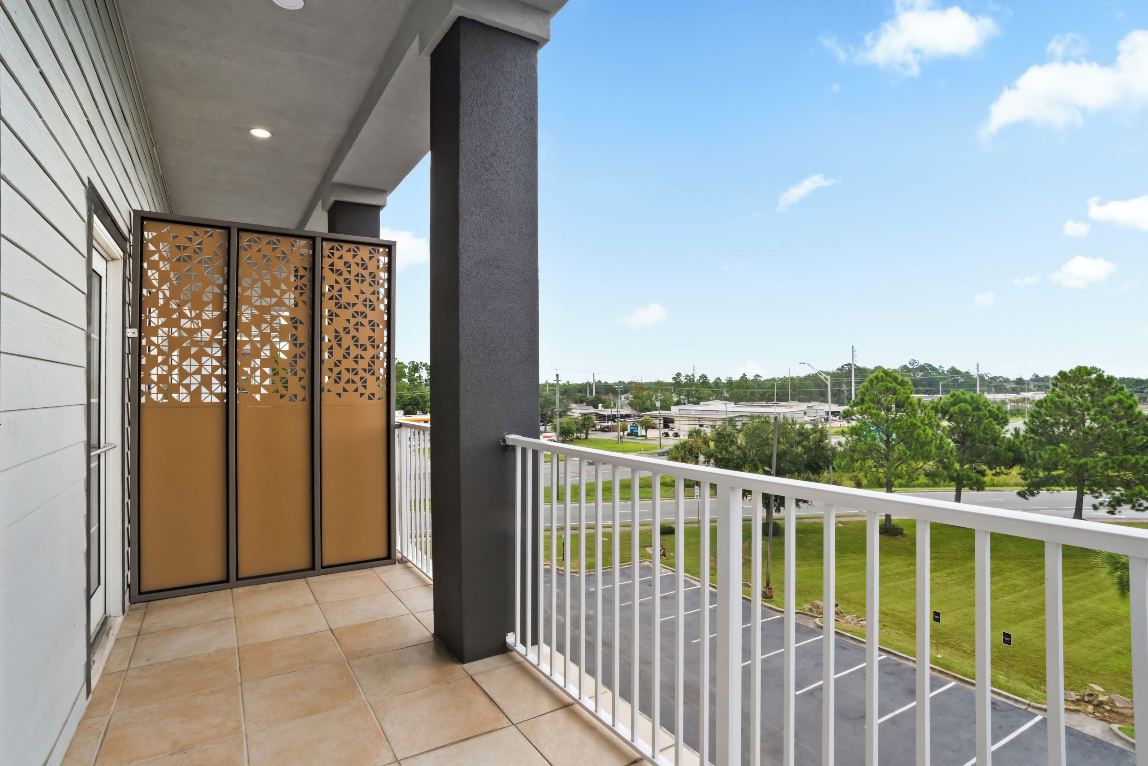 Varanda com vista para um estacionamento e área verde, piso de azulejos e um painel decorativo.