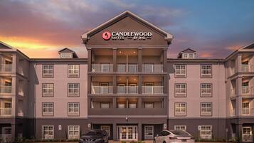A multi-story hotel with a prominent 'CANDLEWOOD SUITES BY IHG' sign, featuring balconies and a parking area with cars.