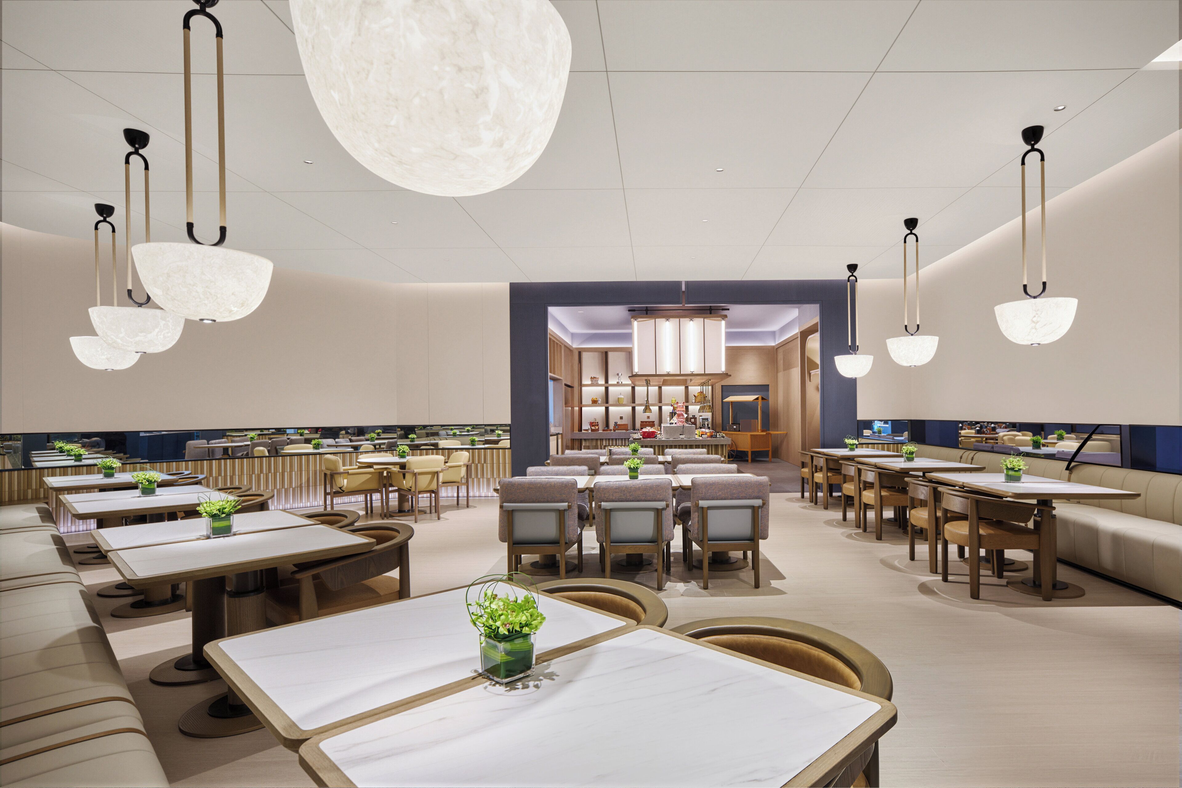 Un restaurante espacioso con numerosas mesas y sillas, un gran candelabro en el centro y vistas al área de la cocina.