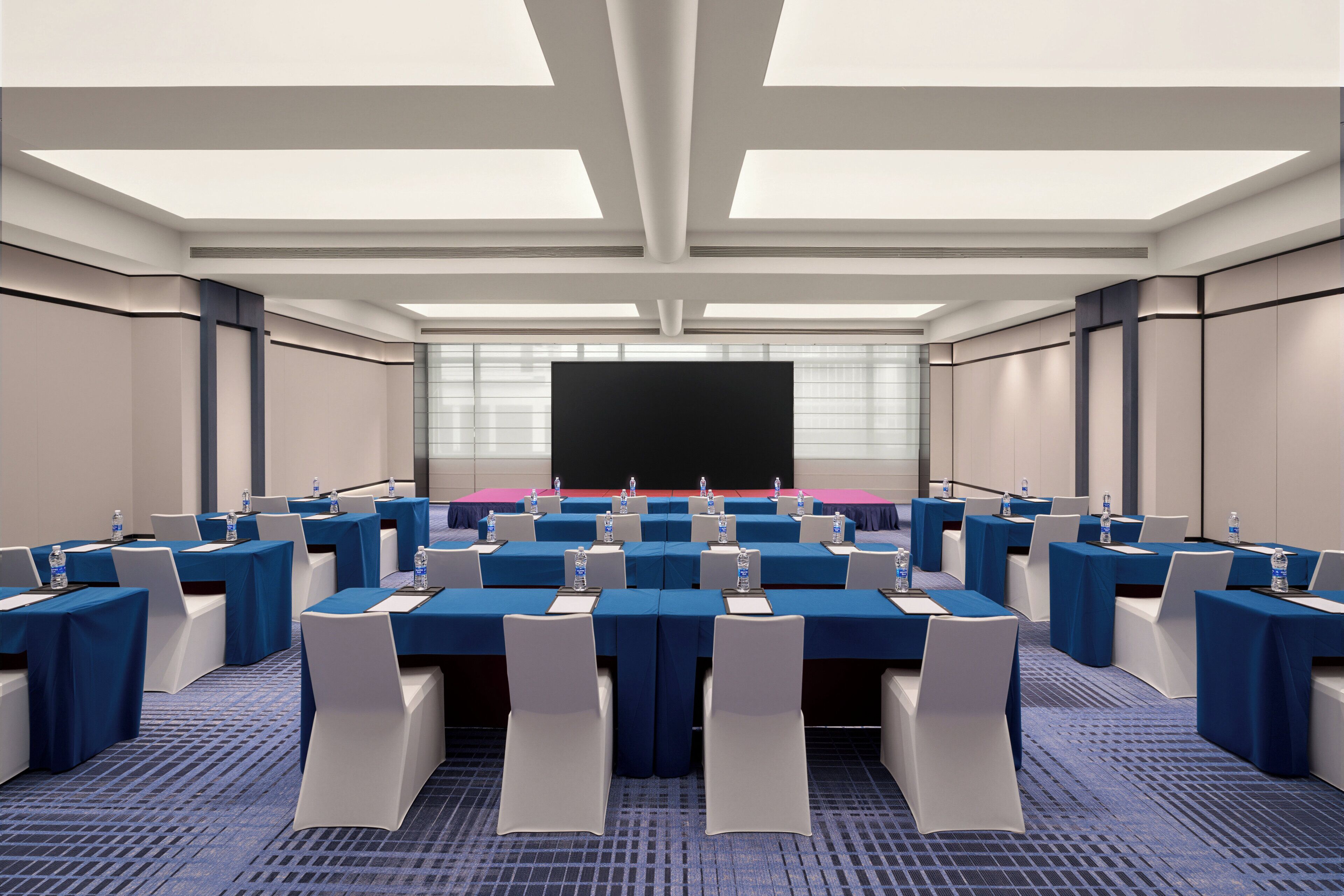 Une salle de conférence équipée de plusieurs tables, de chaises et d’un grand écran situé au fond de la pièce.