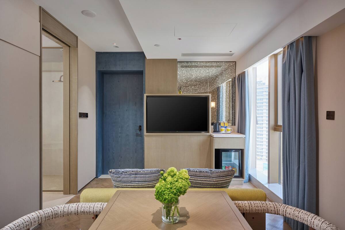 A modern living room with a flat-screen TV, a sofa, a dining table, and a vase of flowers.
