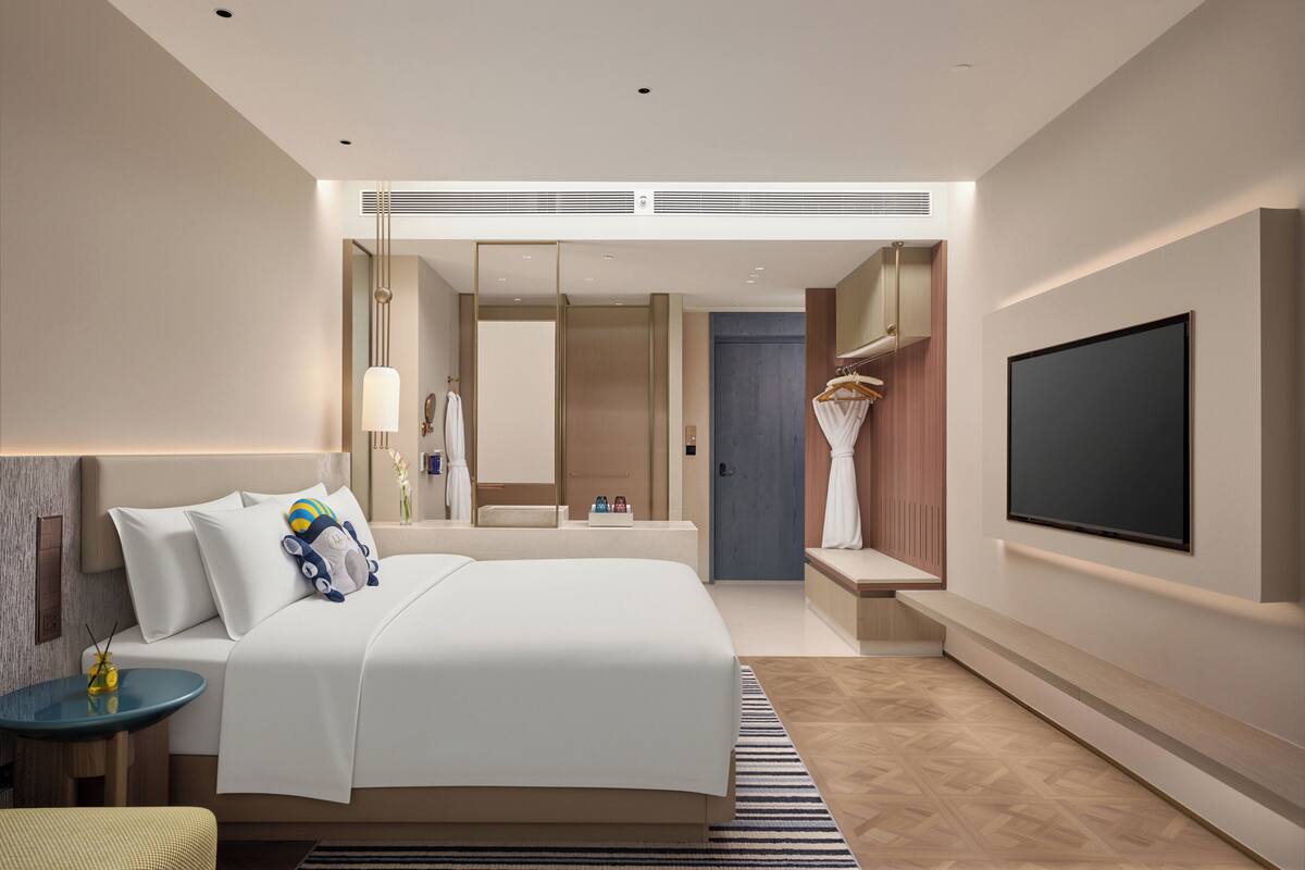 A modern hotel room with a large bed, a TV mounted on the wall, a bedside table, and a mirror.