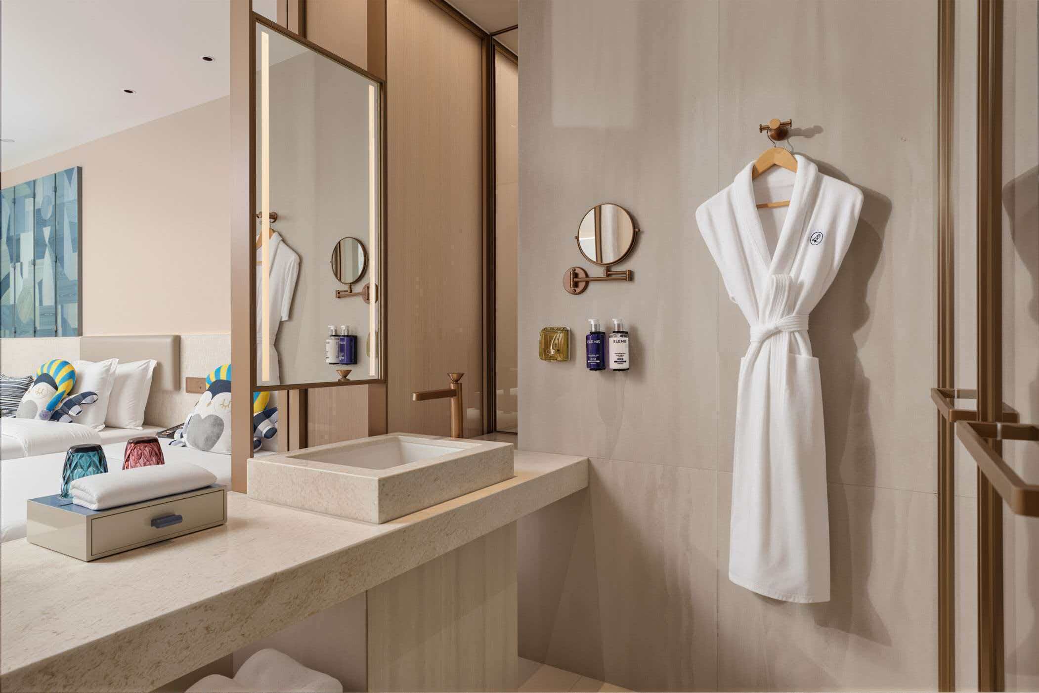 A modern bathroom with a large mirror, a sink, and a robe hanging on the wall.