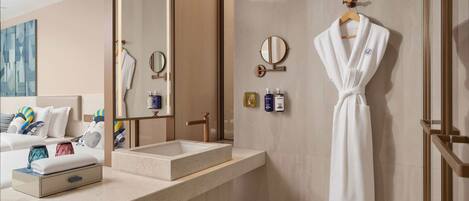 A modern bathroom with a large mirror, a sink, and a robe hanging on the wall.