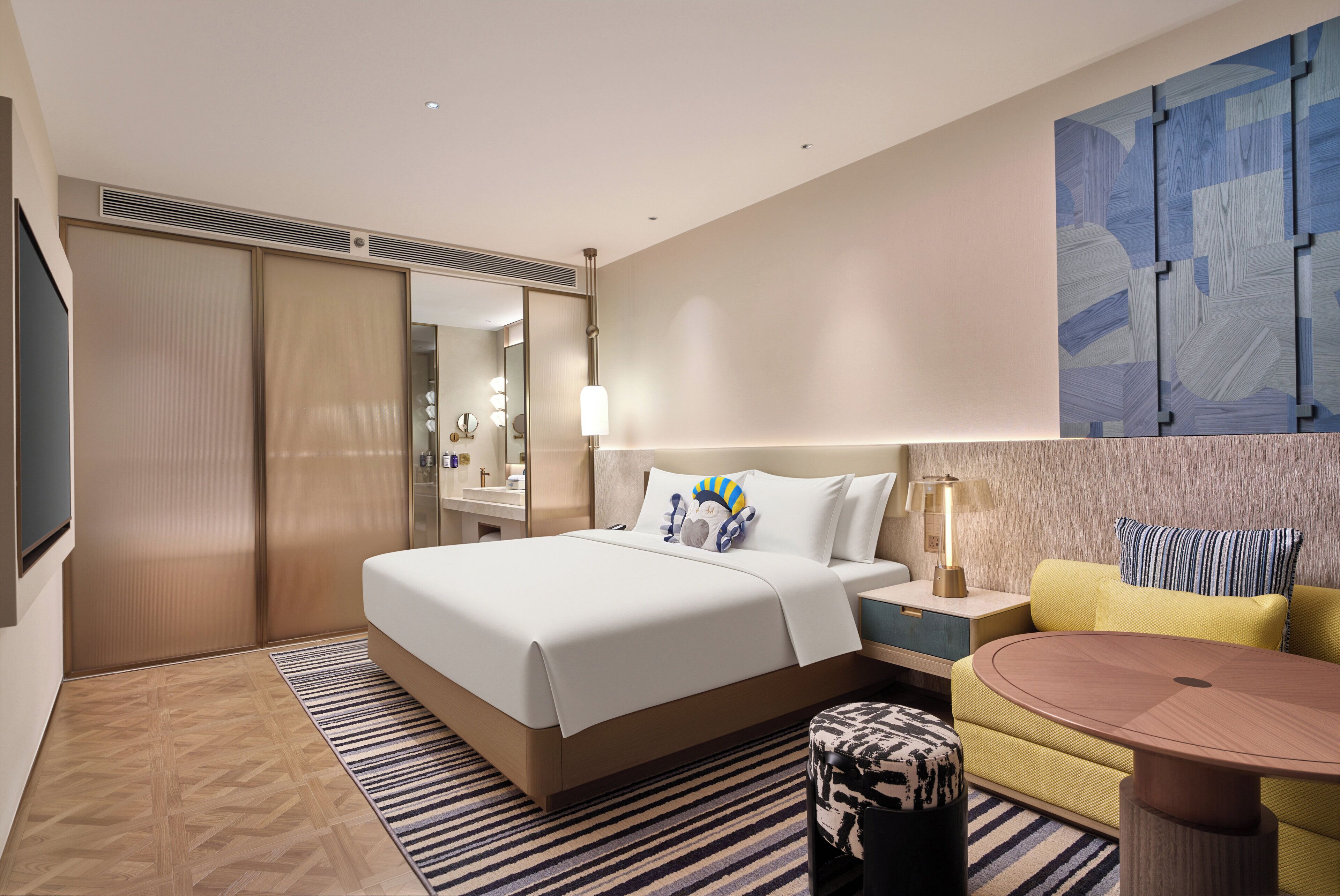 Habitación de hotel con cama, sofá, mesa de centro, espejo y una obra de arte en la pared.