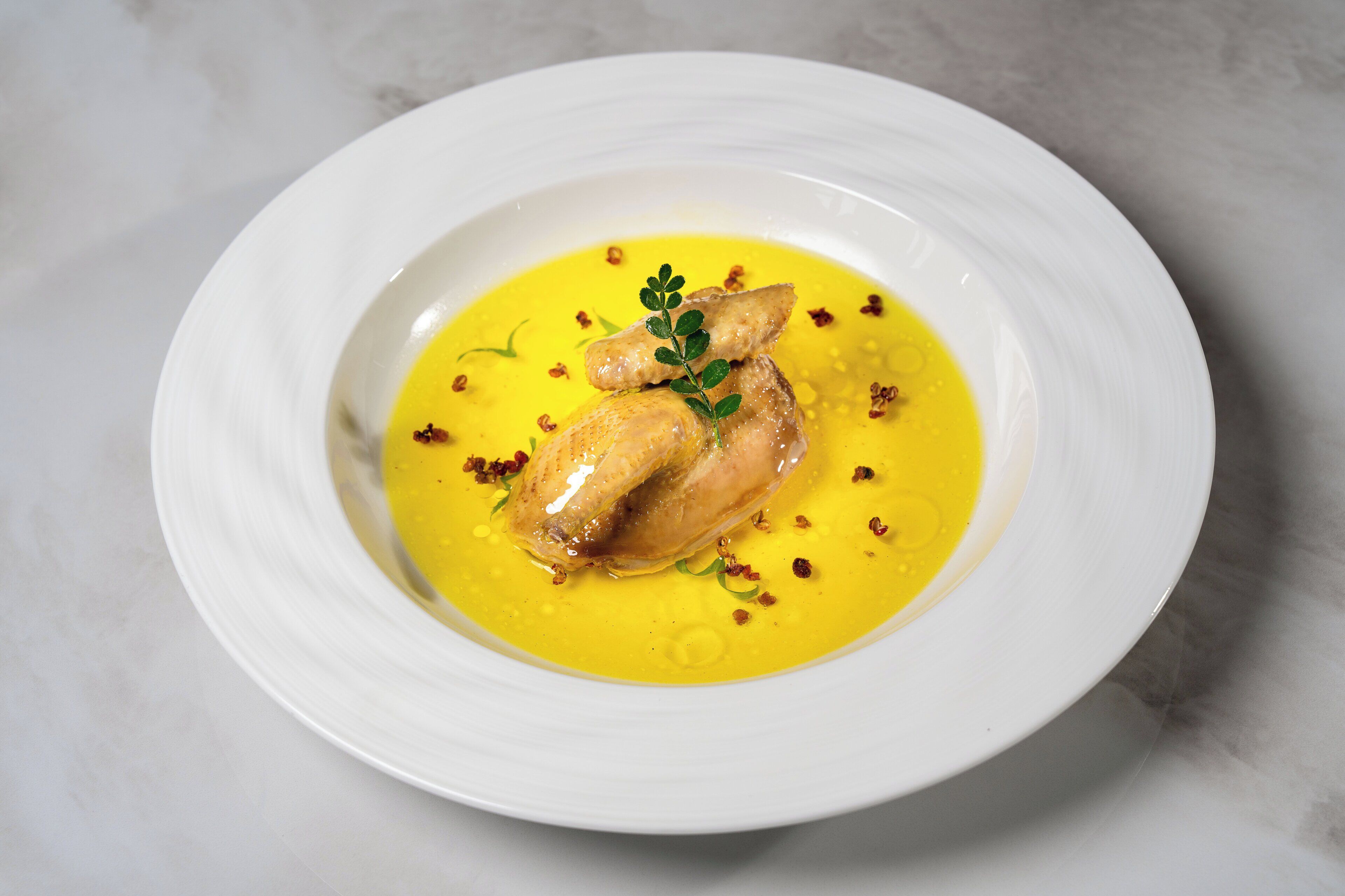 A white plate with a yellow sauce, two pieces of chicken, and a garnish.