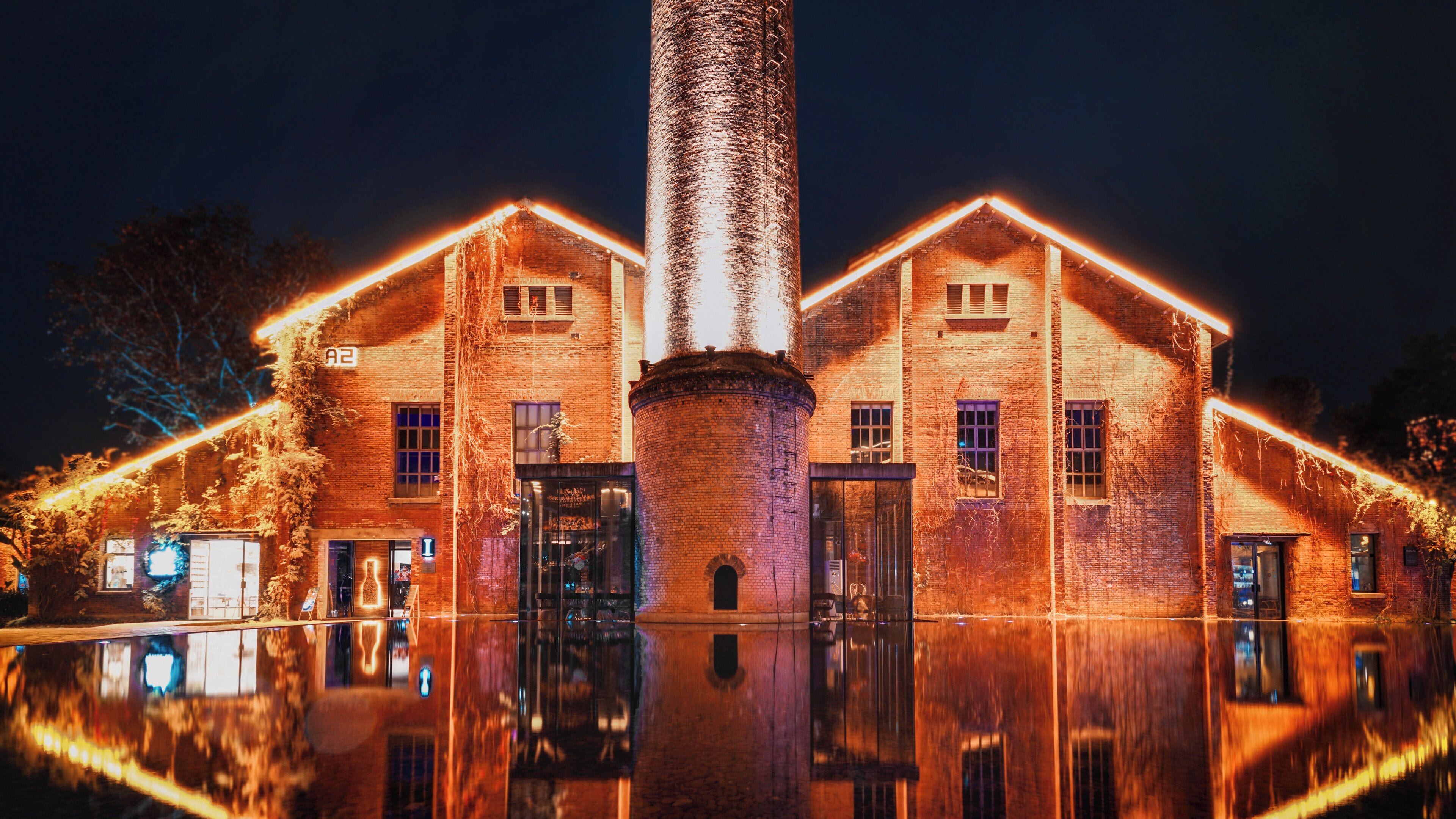 Un edificio in mattoni con una torre centrale, ampie finestre e una superficie d'acqua che si riflette.