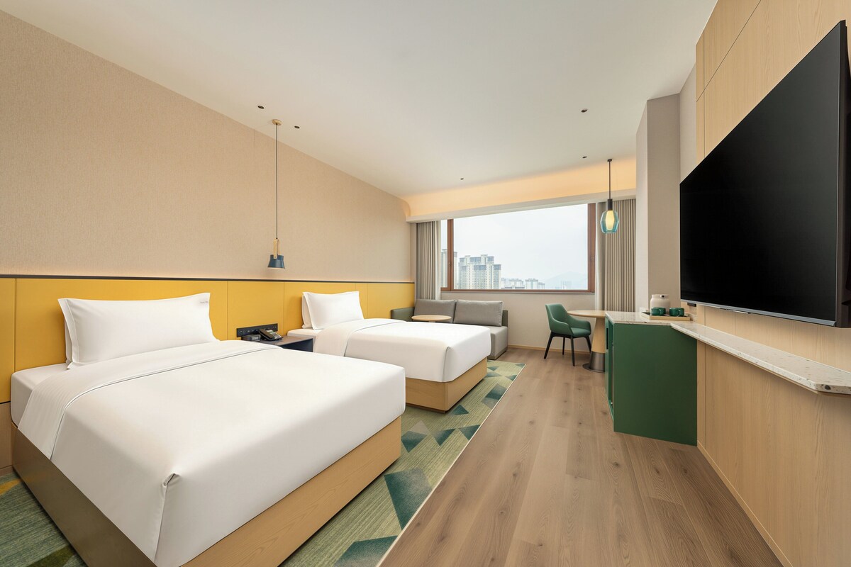 Habitación de hotel con dos camas, un escritorio, un televisor de pantalla plana y vistas a la ciudad.