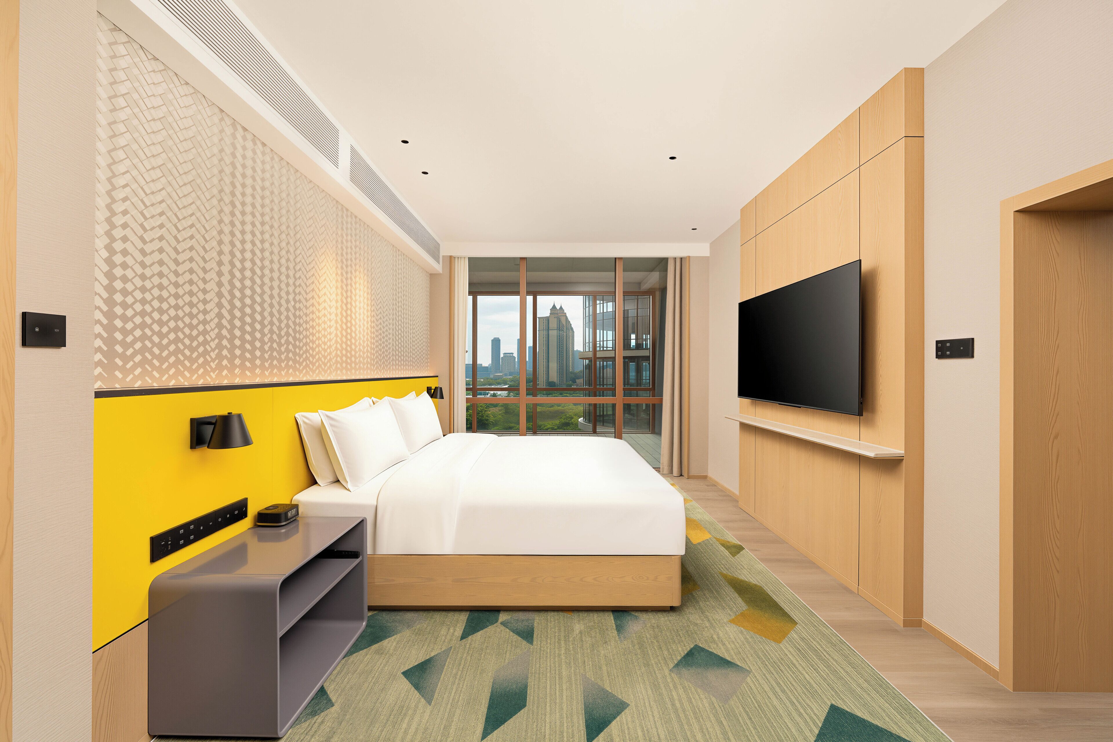 Habitació d'hotel moderna amb llit, televisió, escriptori i una finestra gran que ofereix vista a la ciutat.