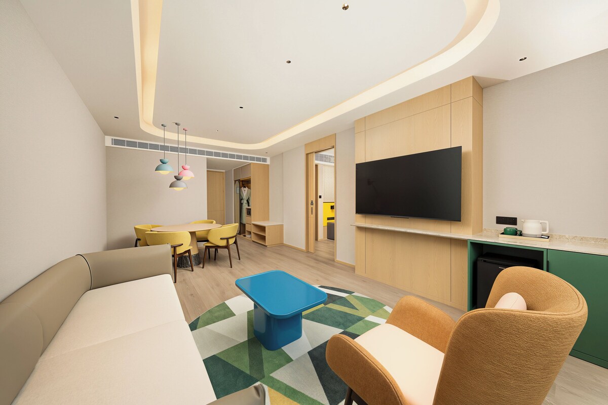 Una habitación de hotel moderna con sofá, mesa de comedor, sillas, televisor de pantalla plana y kitchenette.