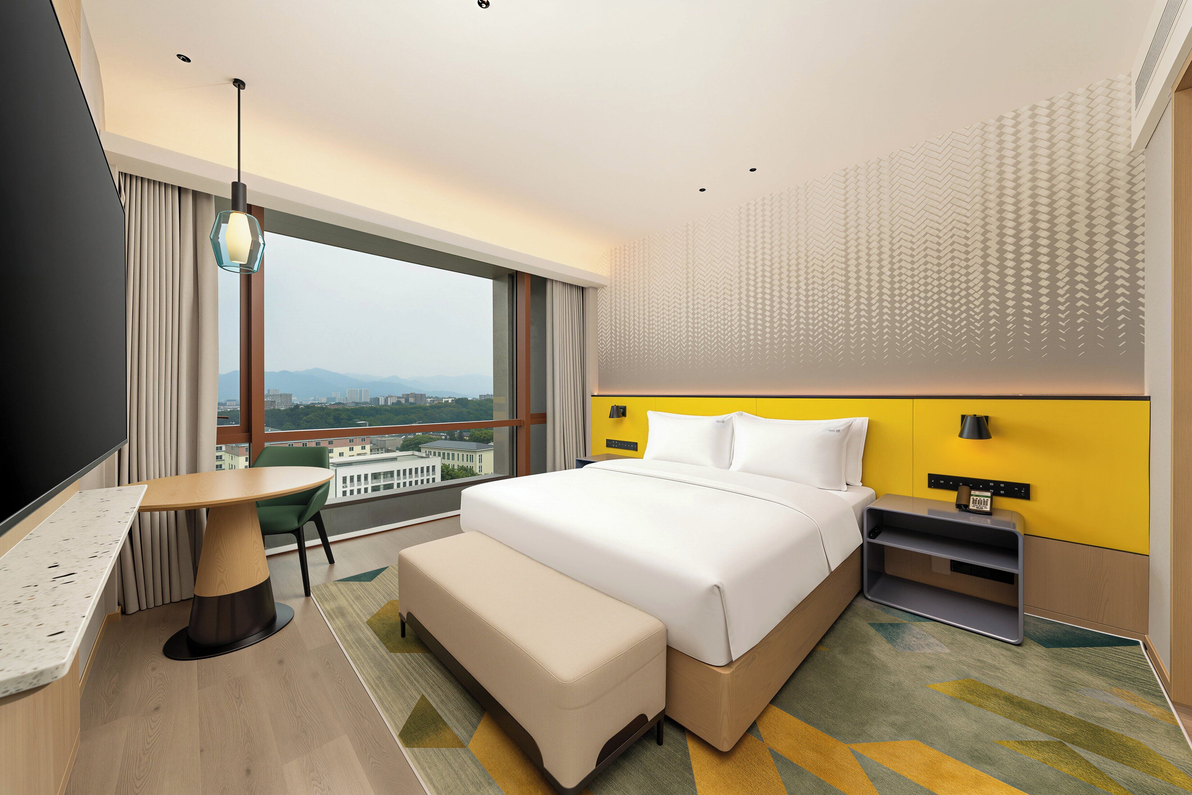 Een moderne hotelkamer met een groot bed, een bureau, een bankje, uitzicht op de stad en een behang met een patroon.