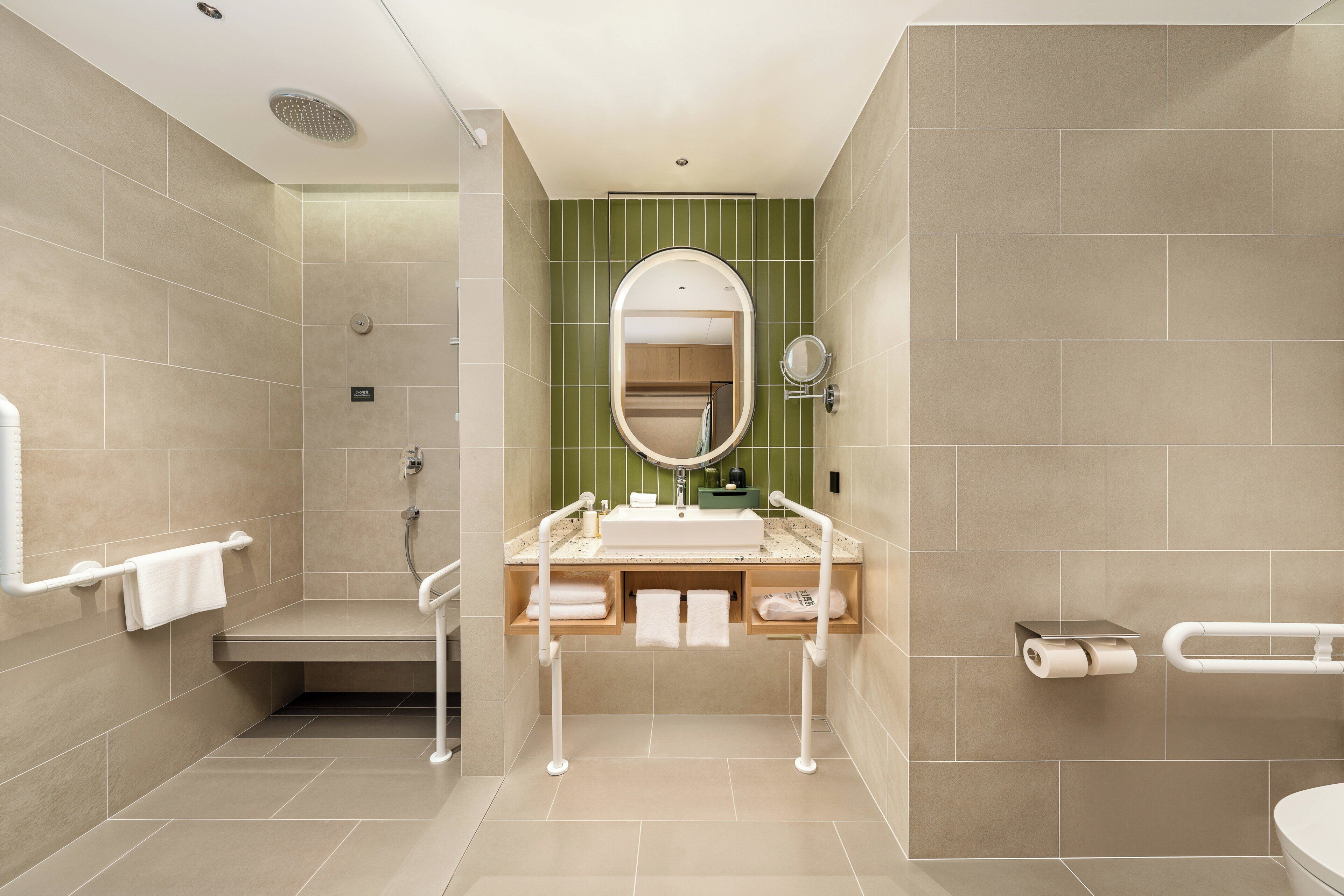 Un baño moderno con ducha, inodoro y lavamanos, equipado con barras de apoyo y un perchero para toallas.