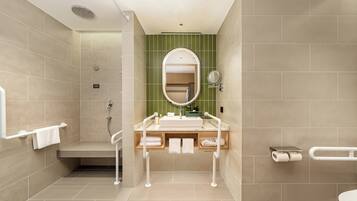 Un baño moderno con ducha, inodoro y lavamanos, equipado con barras de apoyo y un perchero para toallas.
