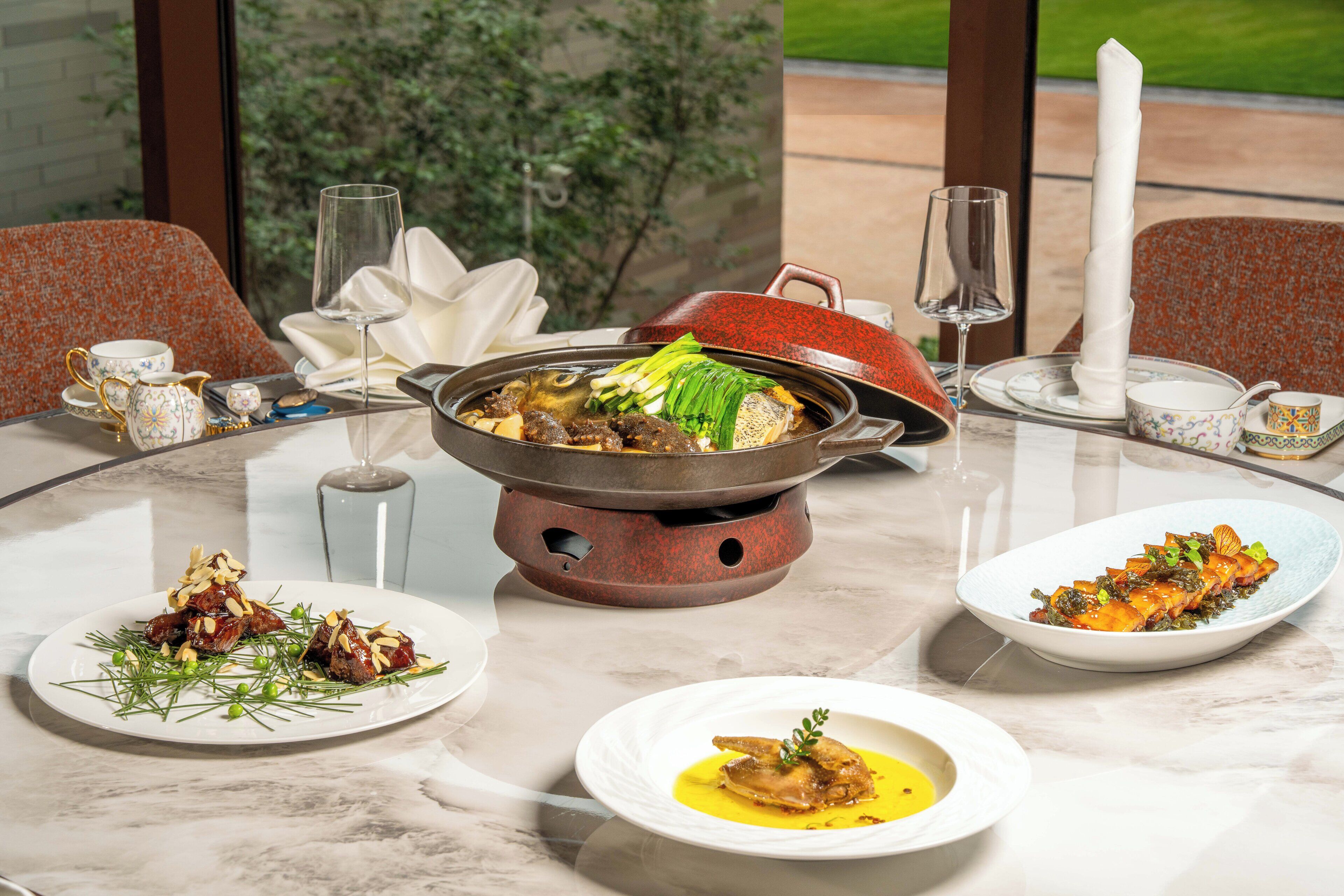 A dining table with a hot pot, plates of food, and a candle.