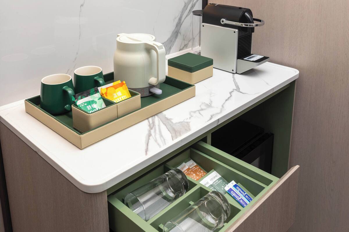 Una encimera de cocina con una cafetera, dos tazas, un hervidor y una bandeja con un sobre de té y una caja de pañuelos.