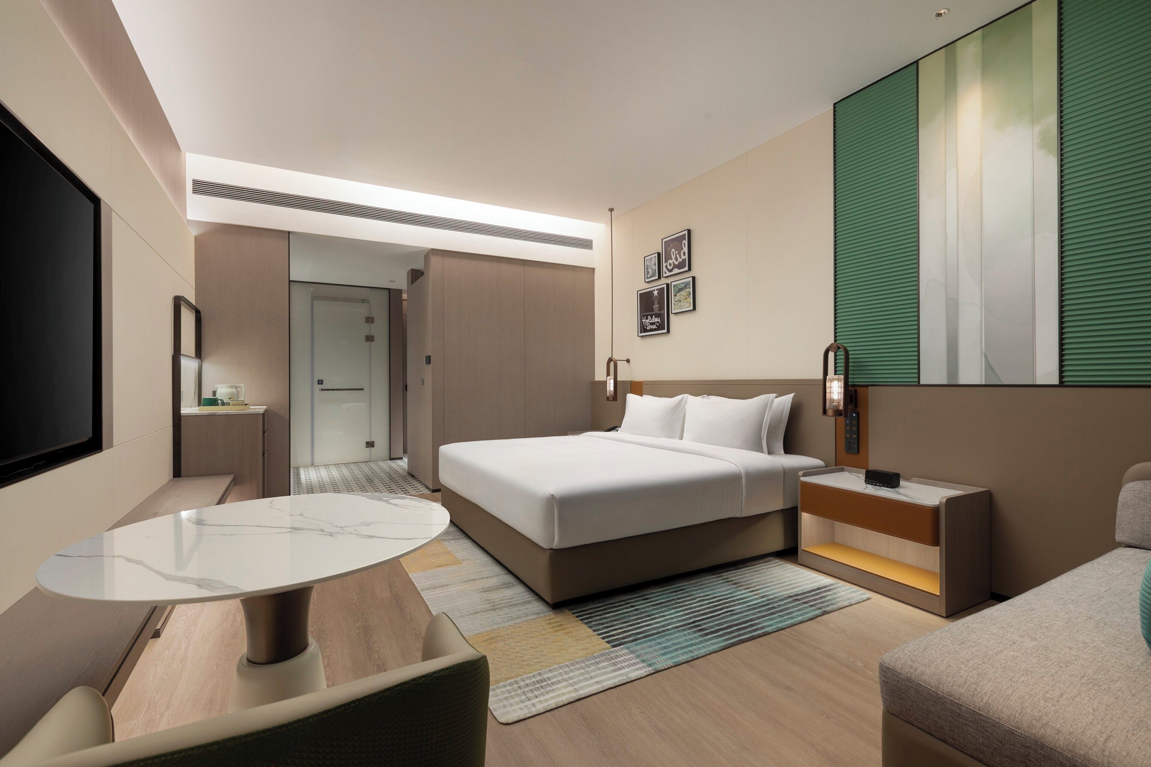 Una habitación de hotel moderna con una cama, un escritorio, una silla, un televisor y un ventanal grande.