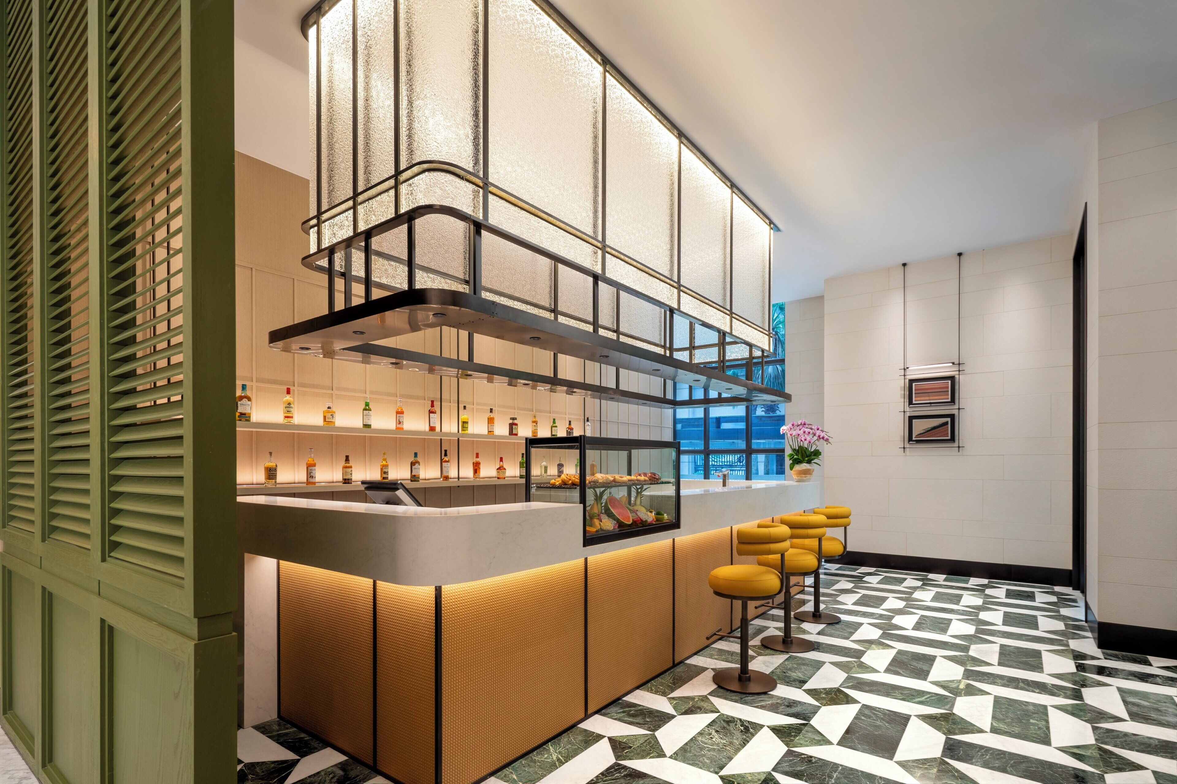 Een moderne bar met een toog, flessenkasten en gele barkrukken.