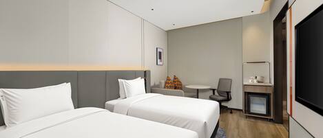 A hotel room with two beds, a small table, a chair, a desk with a computer, and a TV.