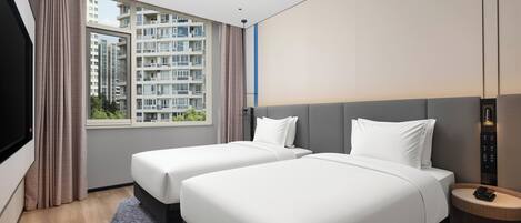 Een hotelkamer met twee bedden, een televisie, een raam met gordijnen en uitzicht op hoogbouw.