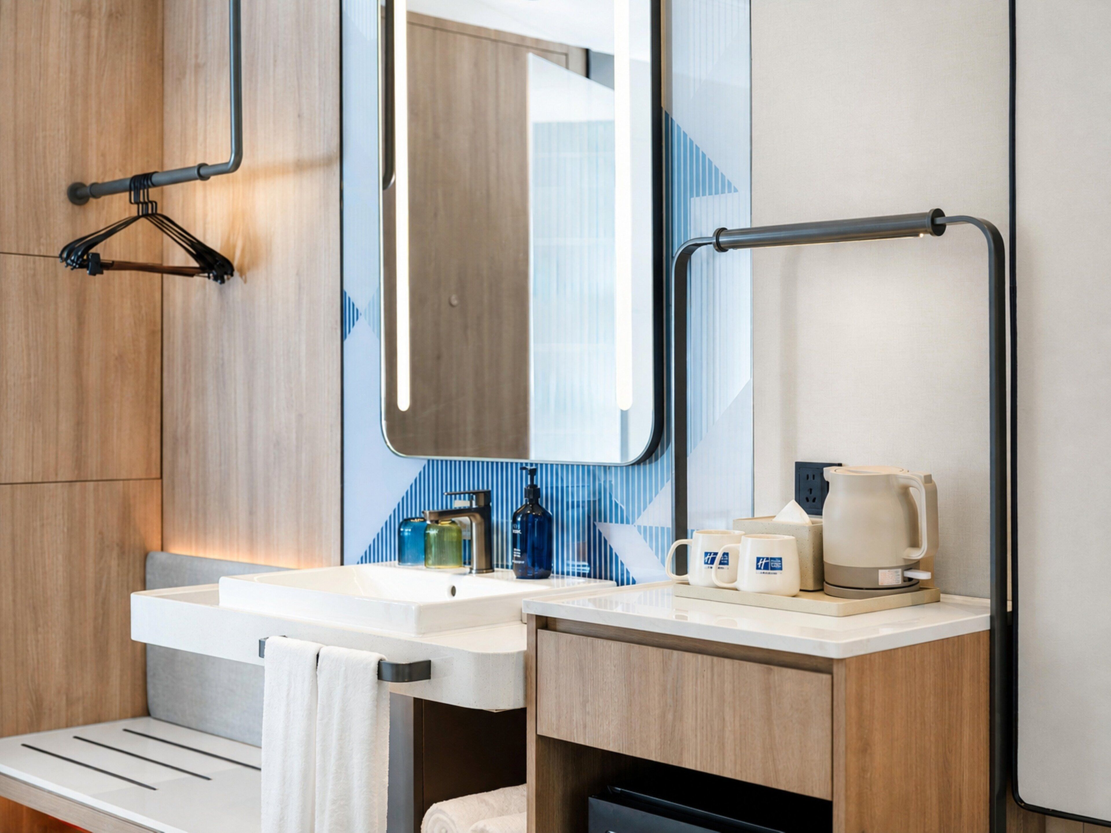 A modern bathroom with a white sink, a mirror, a towel rack, and a coffee maker.