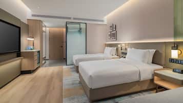A hotel room with two beds, a bedside table, a TV, and a wall-mounted light.