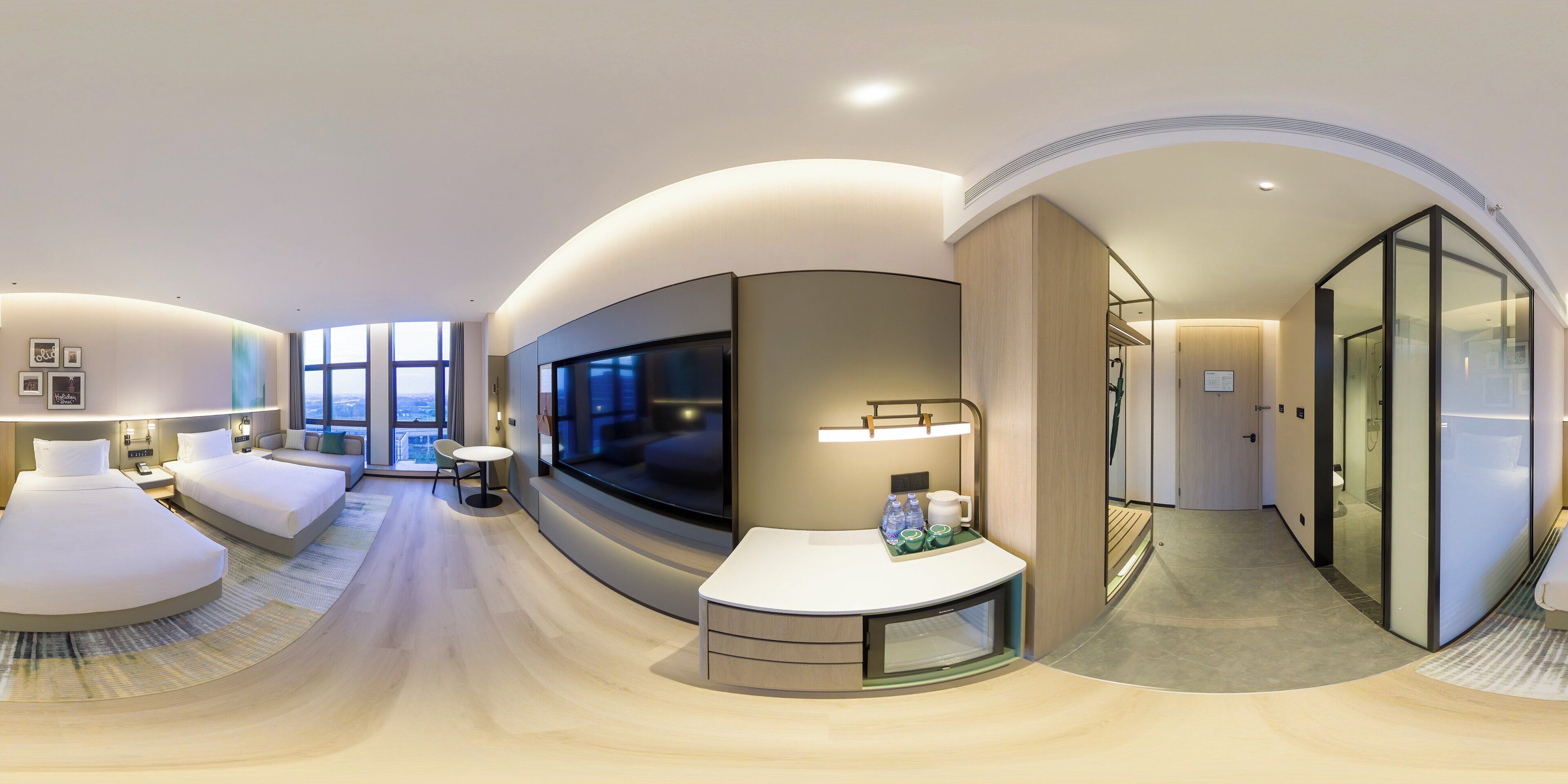 A modern hotel room with a curved layout, a large TV, a seating area, and a view of the city.