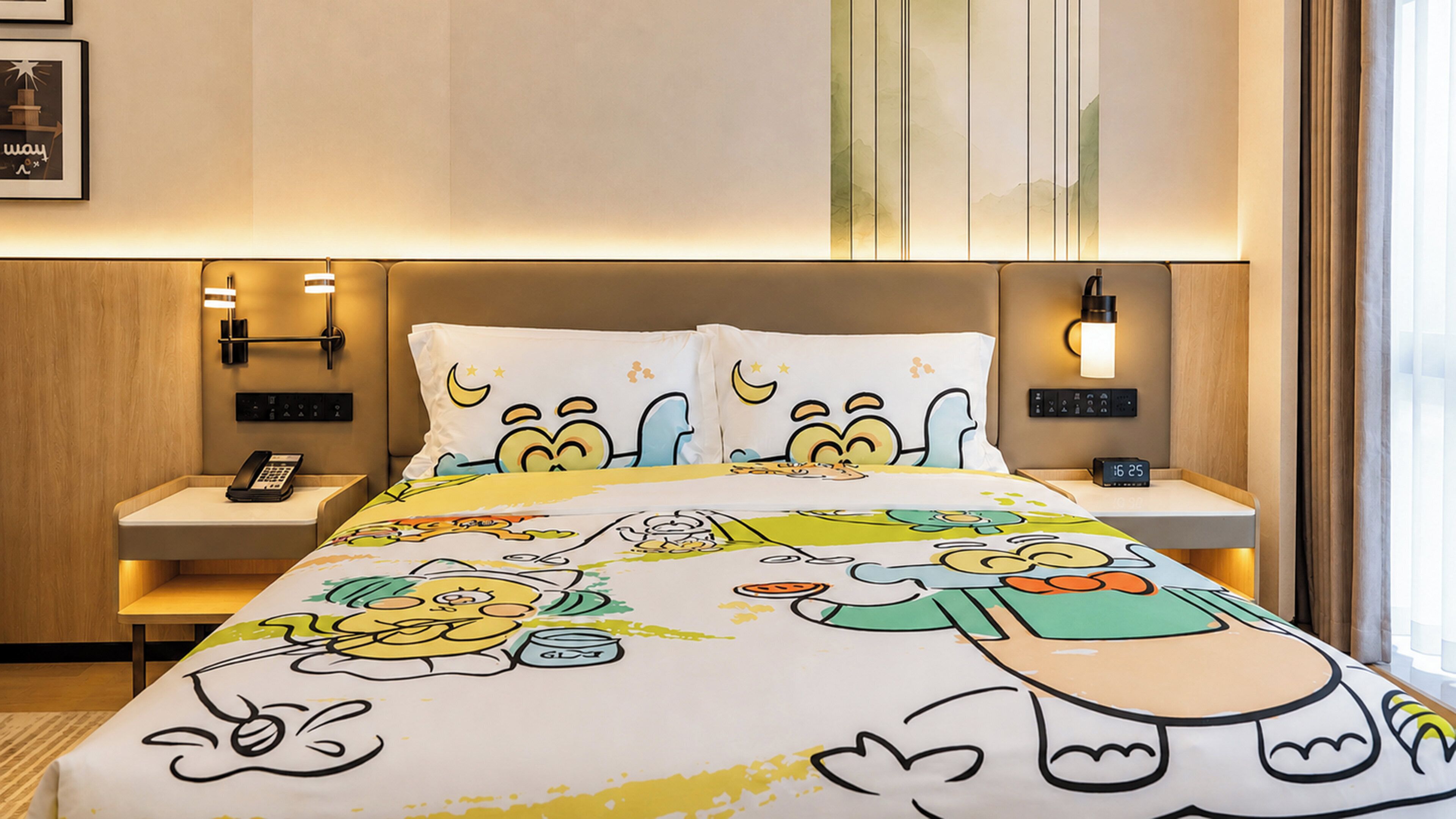 Een hotelkamer met een bed met cartoonafbeeldingen, nachtkastjes met lampen, een telefoon en een digitale klok.