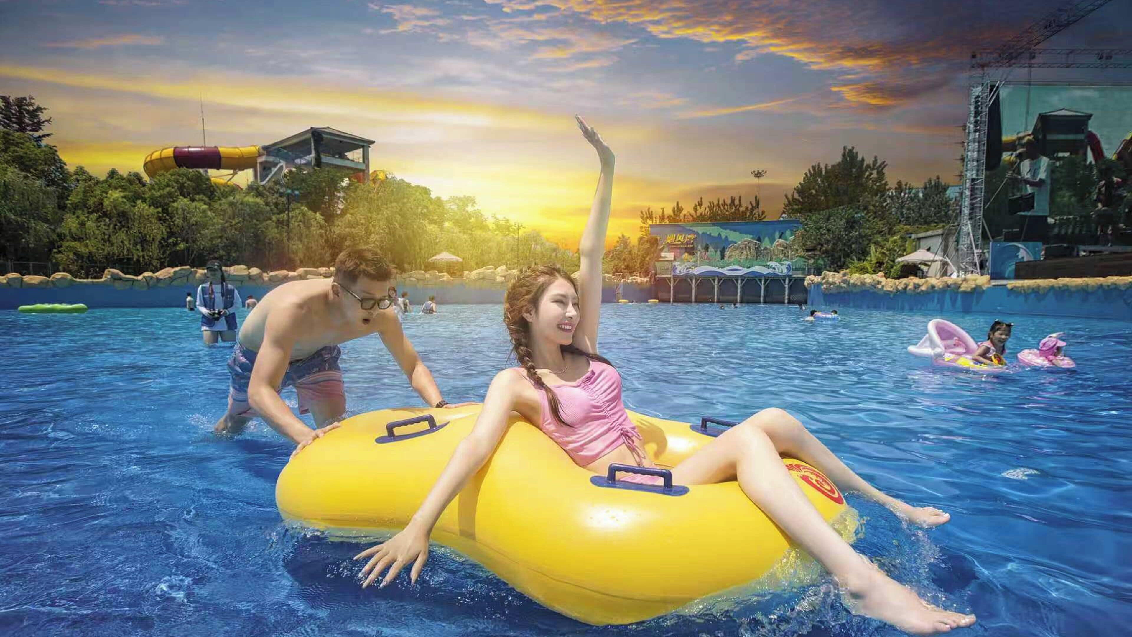 Parque acuático con flotadores inflables, piscina y un atardecer de fondo.