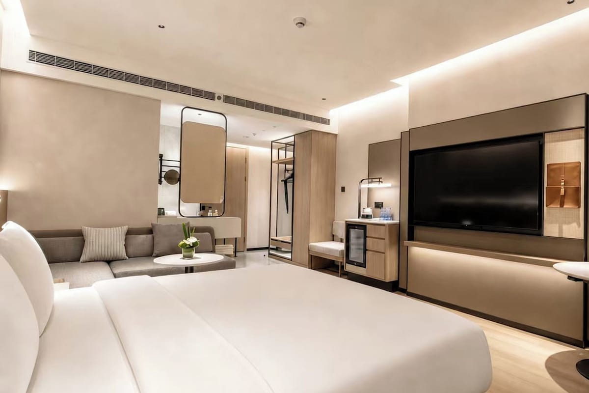 A modern hotel room with a large bed, a TV, a sofa, a desk, and a mirror.