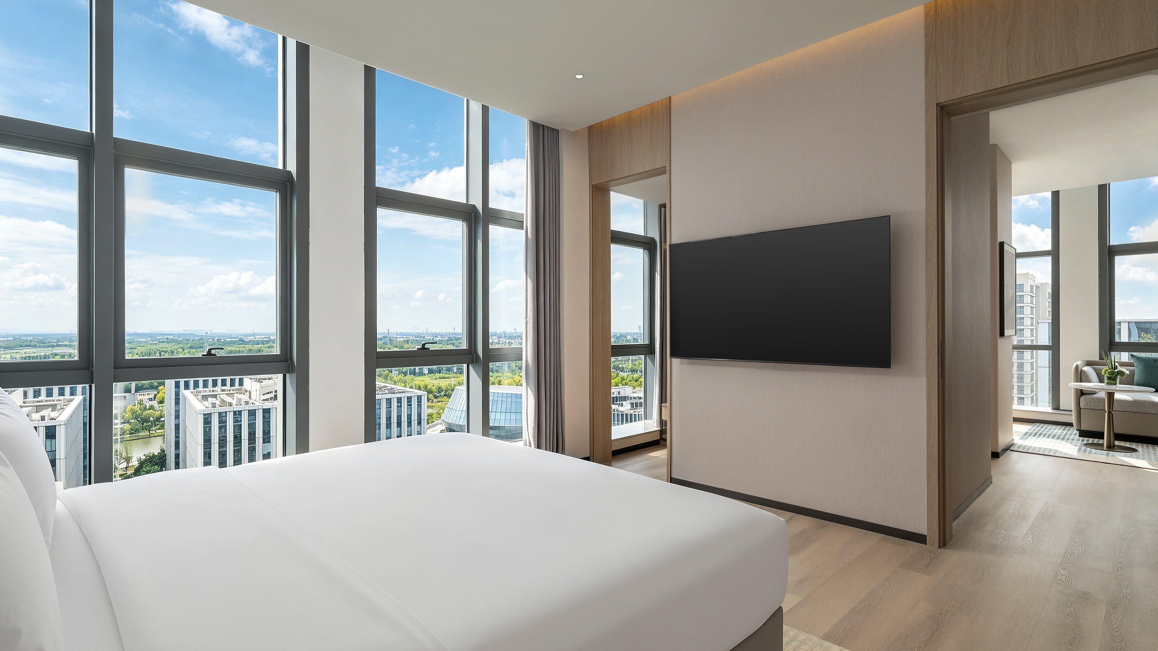 Quarto de hotel moderno com uma cama grande, televisão de tela plana na parede e vista para a cidade através de amplas janelas.