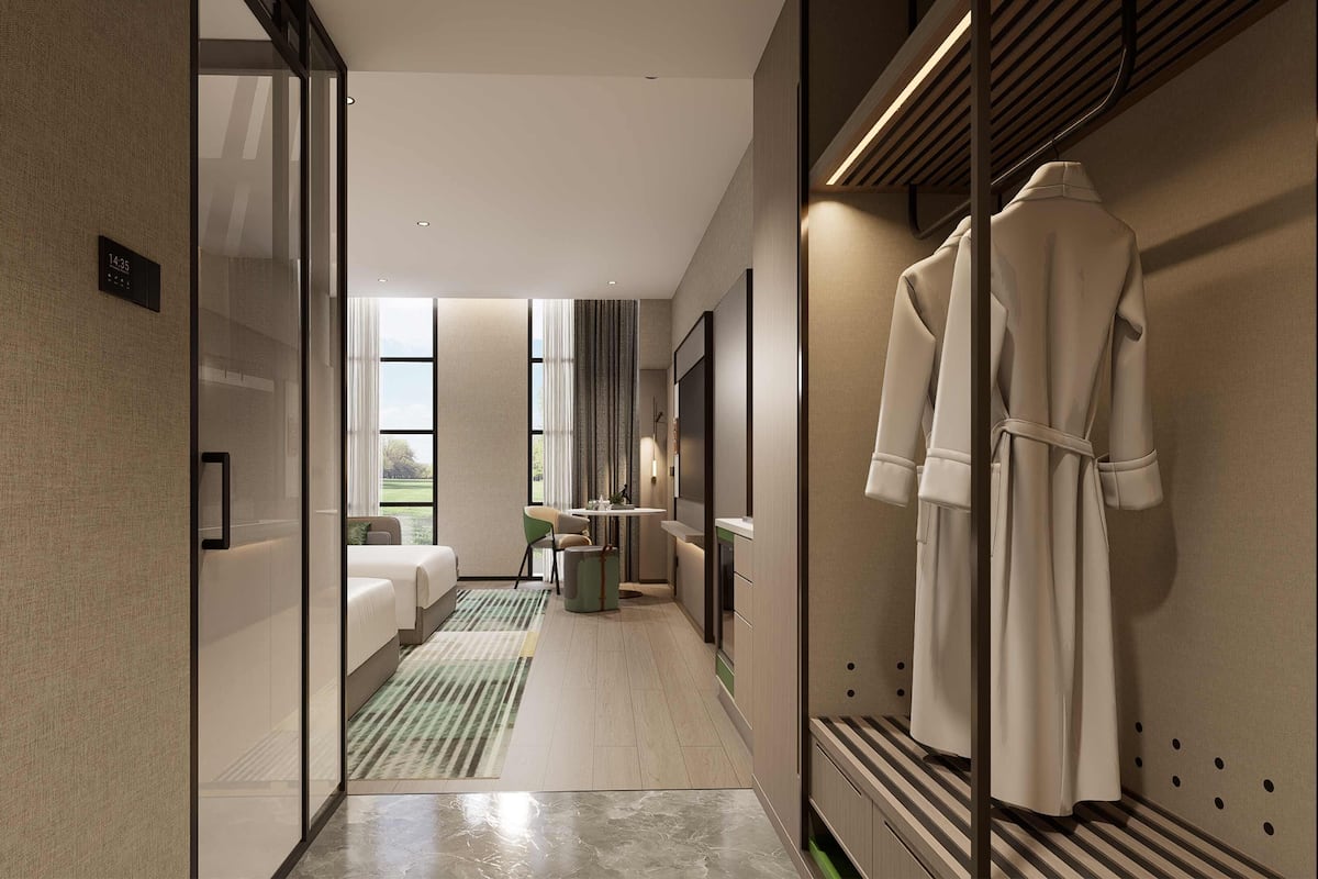 A modern hotel corridor with a bed, a small table, and a robe hanging on the wall.