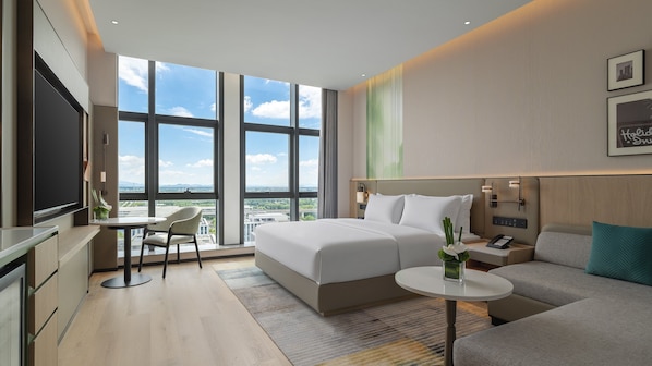 A modern hotel room with a large bed, a desk, a sofa, and a TV.