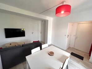 A modern living room with a white sofa, a dining table, and a red pendant light. - La Suite Gilbert | Calme | Centre-ville (Reims)