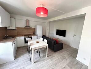 A compact living space with a kitchenette, a dining area, a sofa, and a TV mounted on the wall. - La Suite Gilbert | Calme | Centre-ville (Reims)