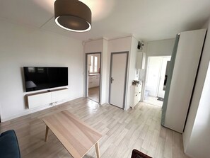 A modern living room with a flat-screen TV, a wooden coffee table, and a light-colored floor. - Le Millésime Gilbert | Duplex | Calme (Reims)