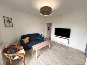 A living room with a sofa, a TV, a coffee table, and a wicker chair. - Le Millésime Gilbert | Duplex | Calme (Reims)