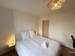 A neatly made bed with white linens, a bedside lamp, and a wall-mounted light fixture. - La Suite Pierret | Centre-ville (Reims)