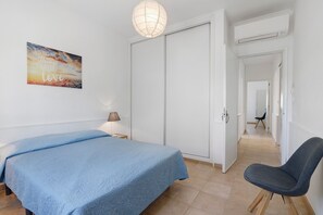 A bedroom with a bed, a chair, a wardrobe, a painting, and a hallway. - Apartment 'Fantástico T2 Albufeira Centro' with Sea View, Wi-Fi and Air Conditioning (Albufeira)