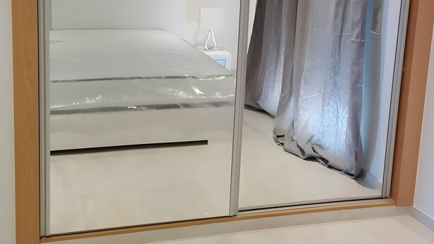 Ein Zimmer mit einer Schiebetür zum Balkon, einem Bett mit weißem Kopfteil, einem Nachttisch mit Lampe und einer Wandleuchte.